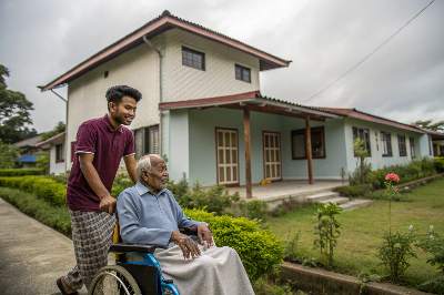 A caregiver taking an elderly guy for a evening walk on a wheel chair.