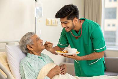 A Patient Care Attendant (PCA) helping a patient eat food with a spoon.
